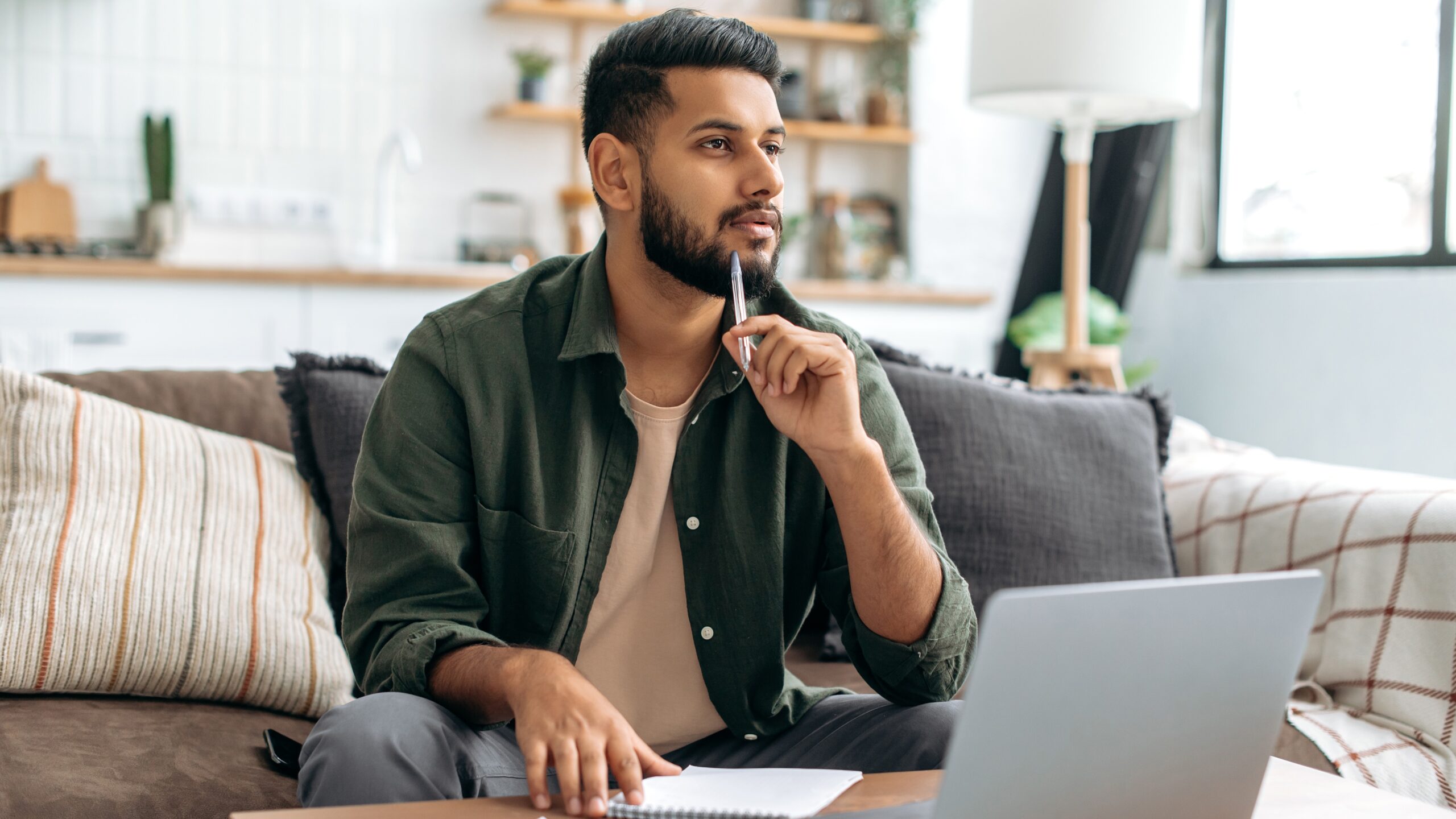 A thoughtful young professional compares housing costs on a desktop, weighing the pros and cons of renting versus buying with side-by-side charts.