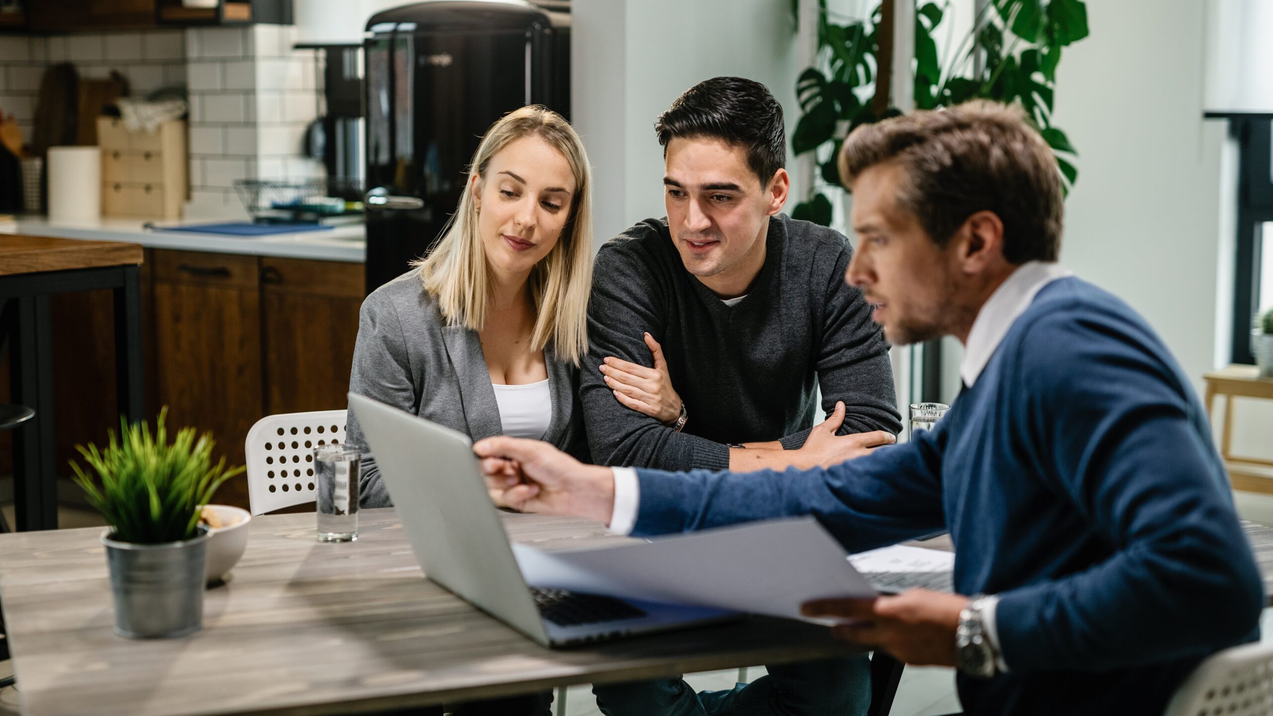 A couple sits with a mortgage advisor in a bright office, reviewing budget limits and exploring how much home they can comfortably afford.