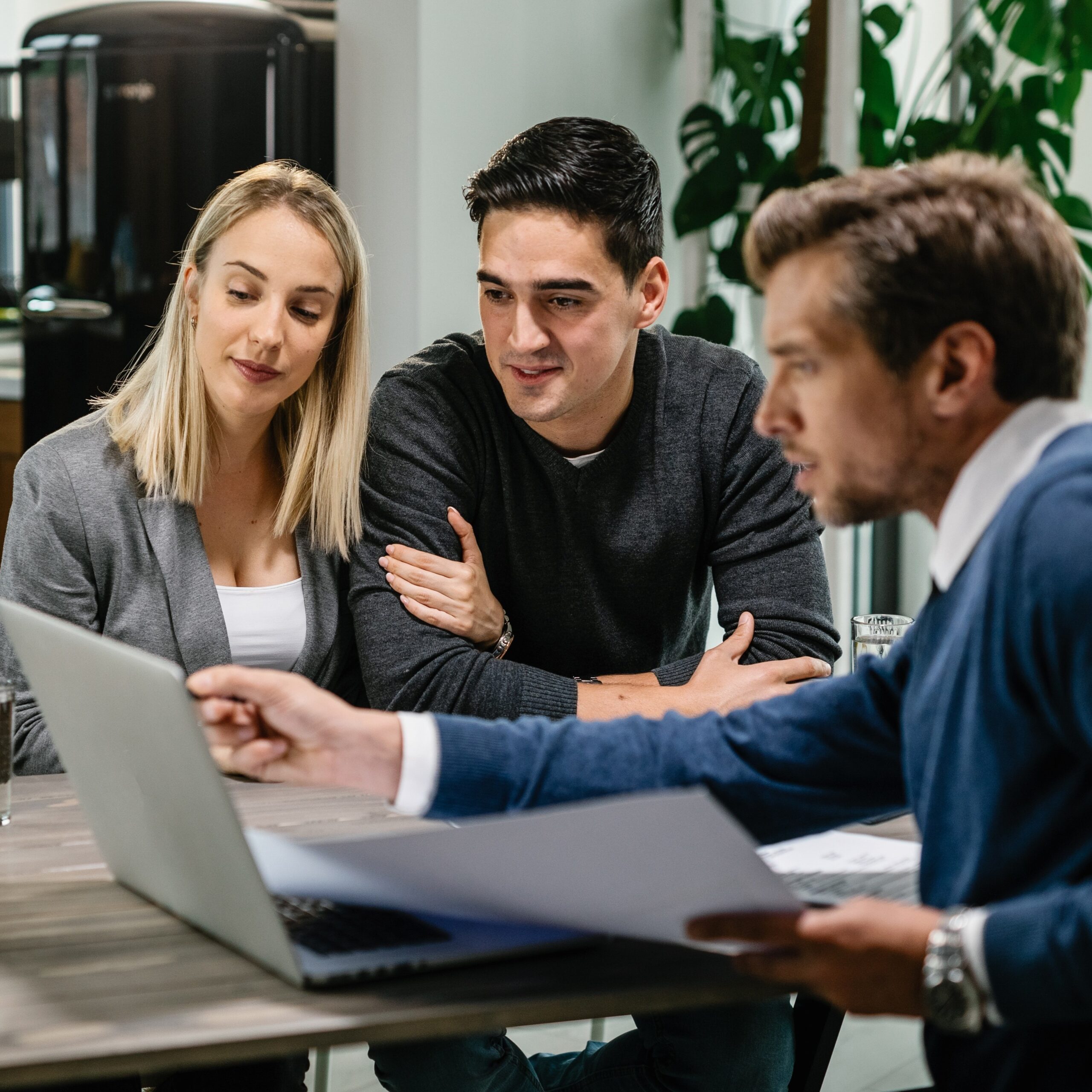 A couple sits with a mortgage advisor in a bright office, reviewing budget limits and exploring how much home they can comfortably afford.