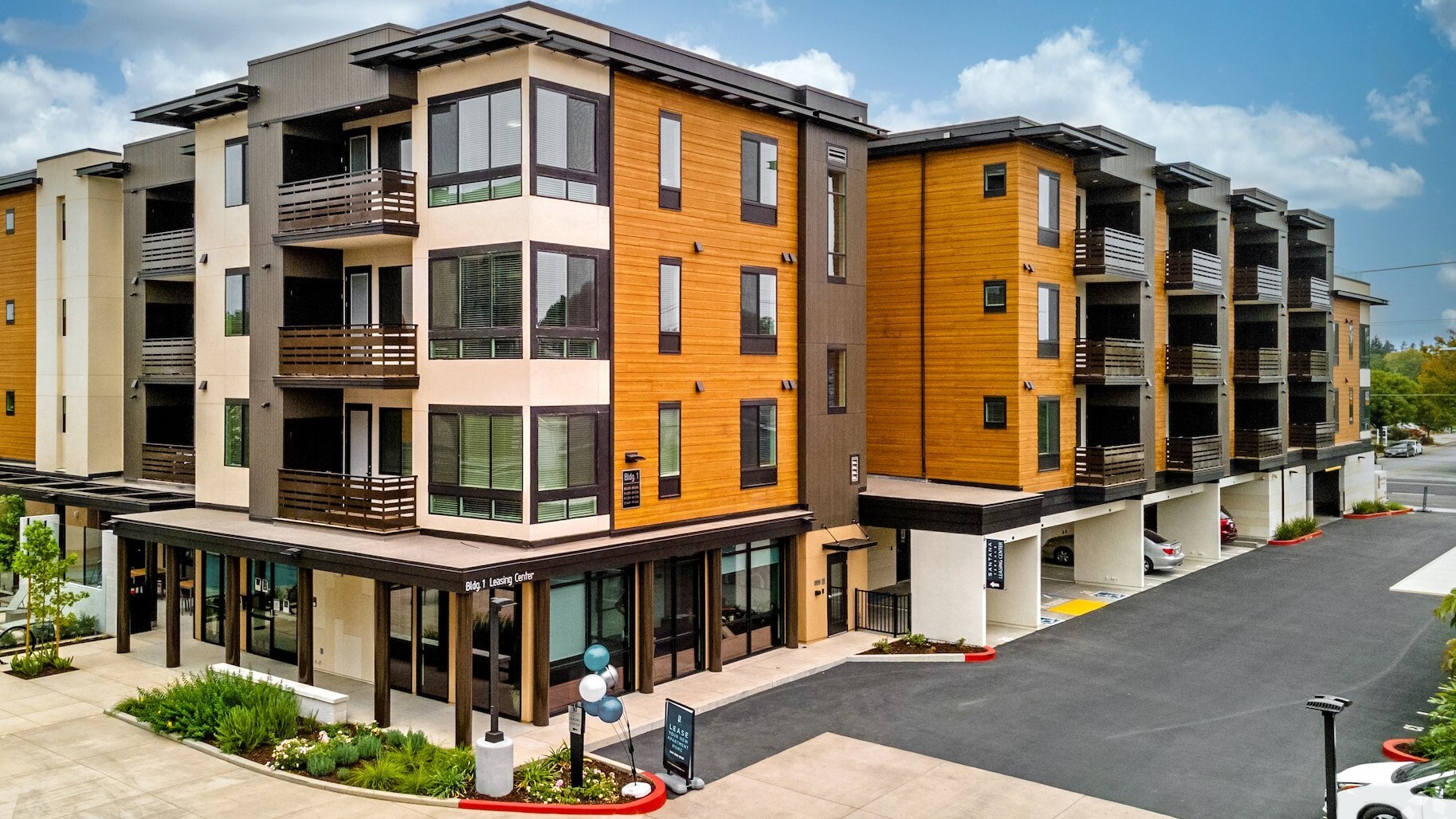 Modern mid-rise apartment complex with wood and stucco exterior, leasing center at street level, and covered parking—represents a turnkey investment property.