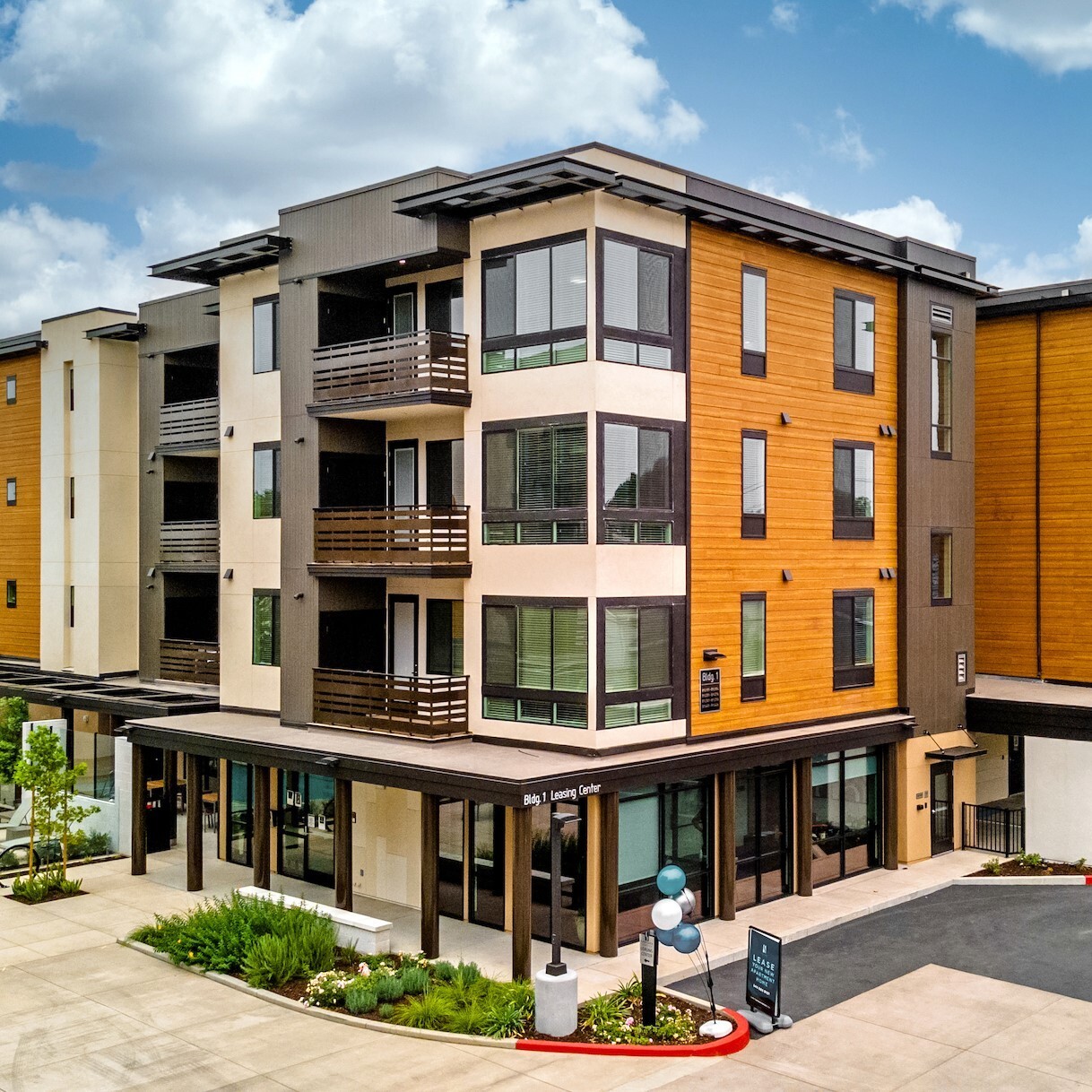 Modern mid-rise apartment complex with wood and stucco exterior, leasing center at street level, and covered parking—represents a turnkey investment property.