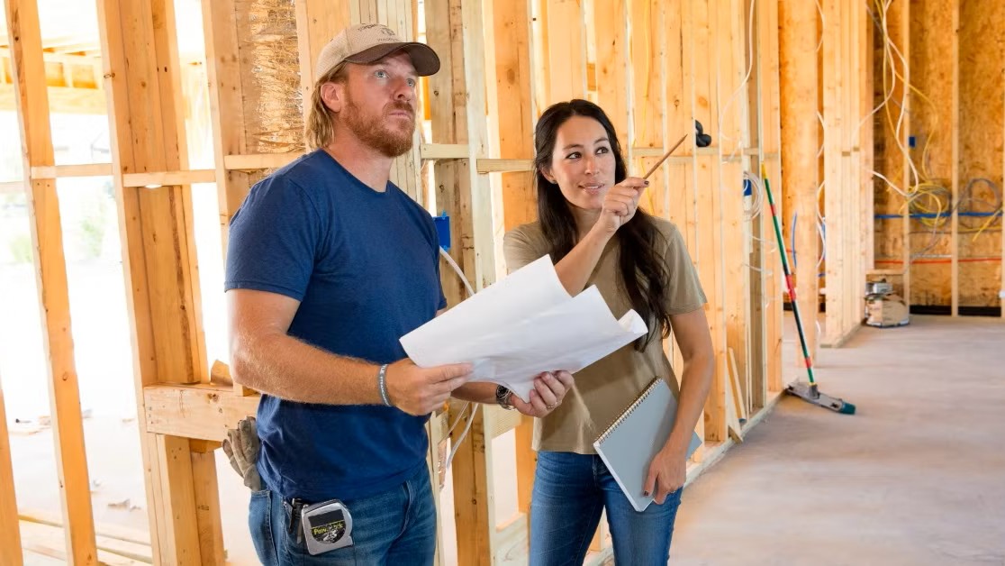 A man and woman review renovation plans inside a property under construction, discussing upgrades that will enhance value and appeal—symbolizing strategic improvements that drive return on investment in real estate.