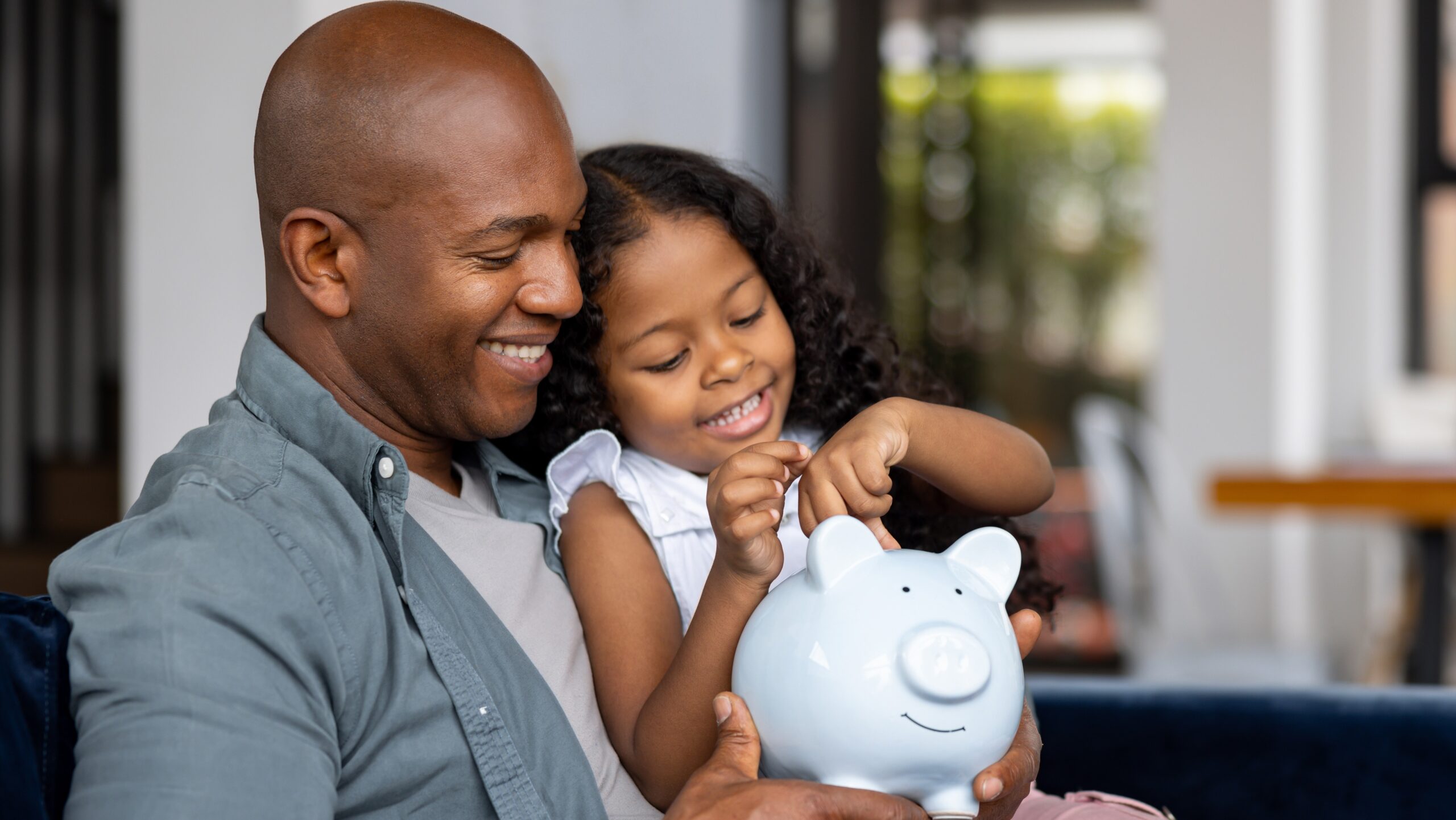 A father and daughter share a joyful moment while saving money together, symbolizing the importance of financial literacy, planning, and building a secure future for the next generation.