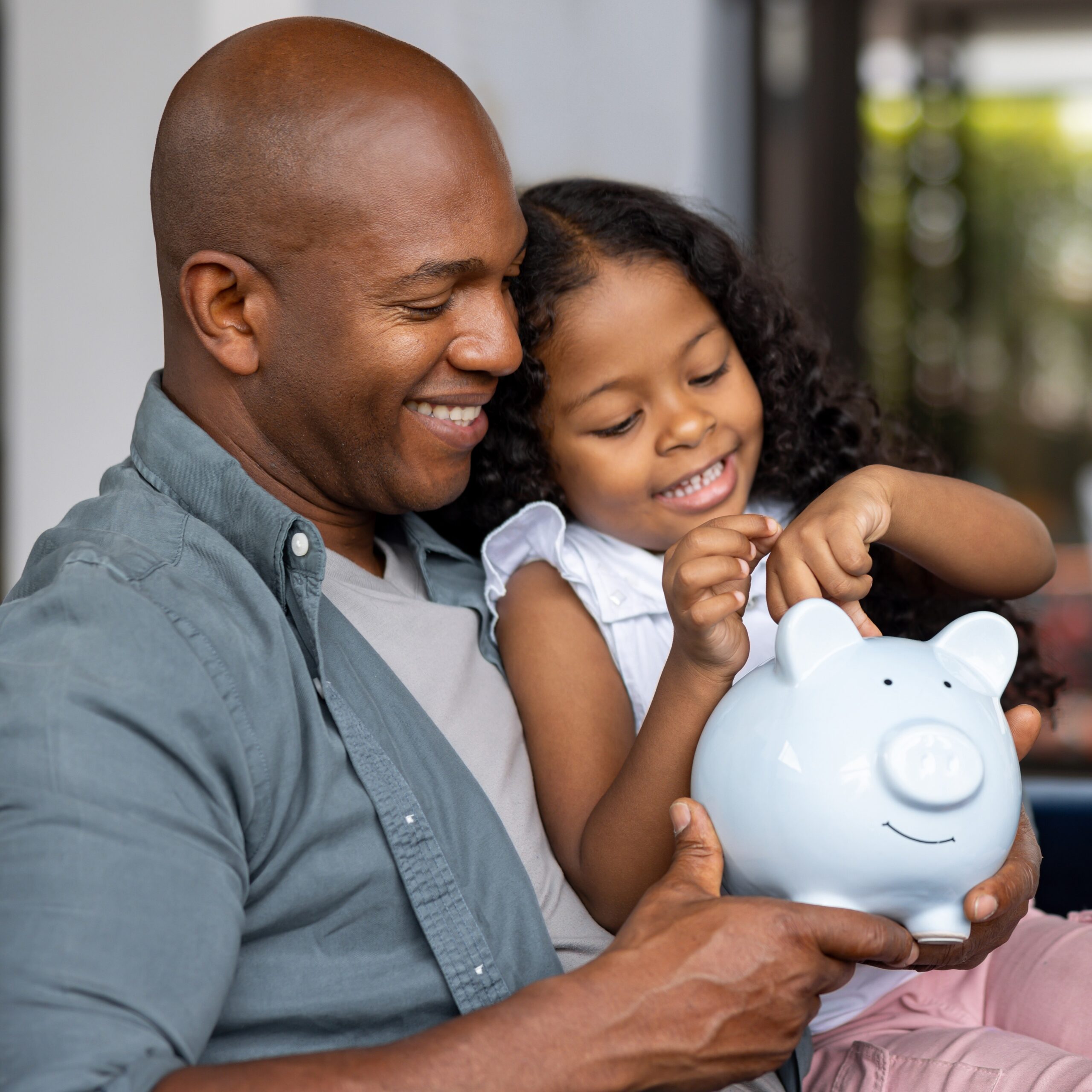 A father and daughter share a joyful moment while saving money together, symbolizing the importance of financial literacy, planning, and building a secure future for the next generation.